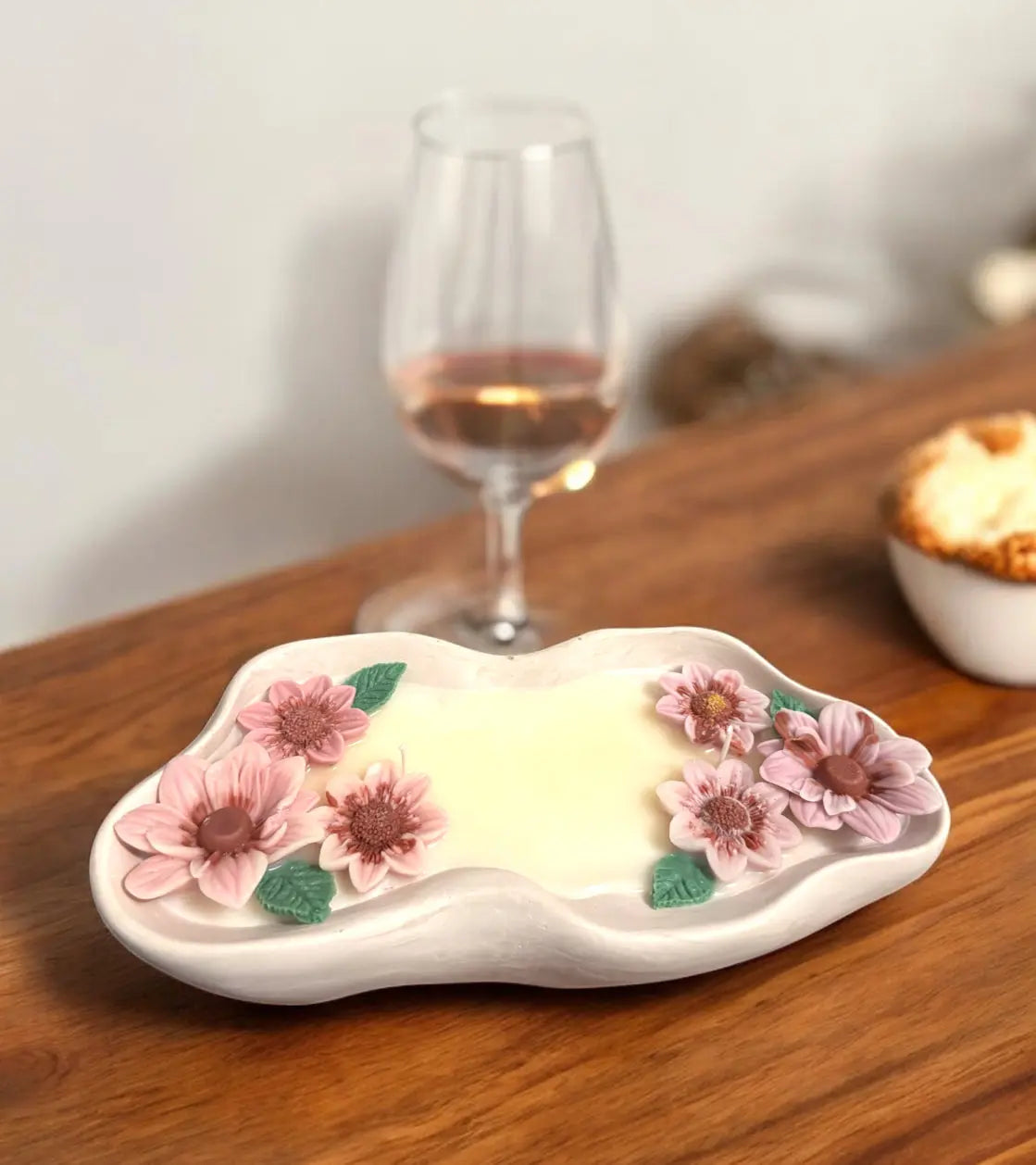Handmade flower candle in unique container with pink and purple flowers, set on a wooden table near a glass of rosé wine.