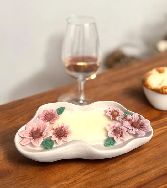 Handmade flower candle in unique container with pink and purple flowers, set on a wooden table near a glass of rosé wine.
